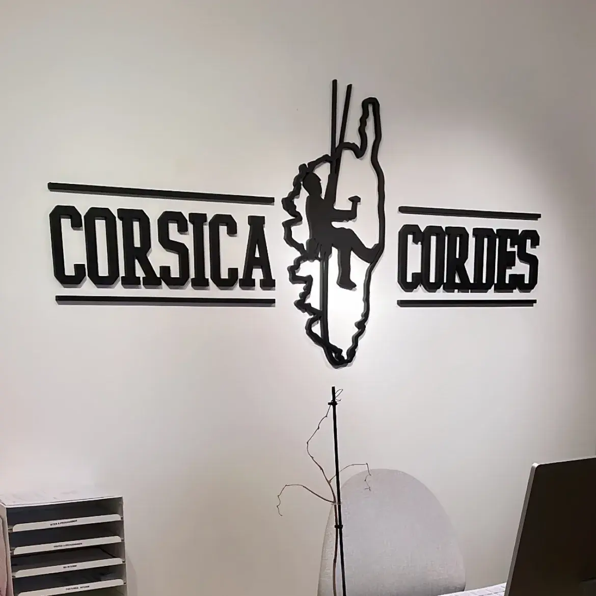 Lettrage noir découpé avec la silhouette d'un grimpeur, posé en relief sur le mur blanc d'un bureau