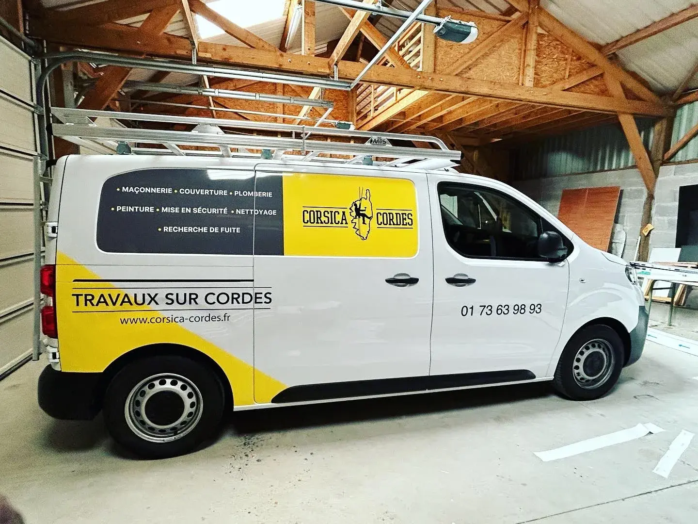 Utilitaire blanc habillé d'un marquage jaune et noir sur les flancs, galerie de toit, garé dans un hangar