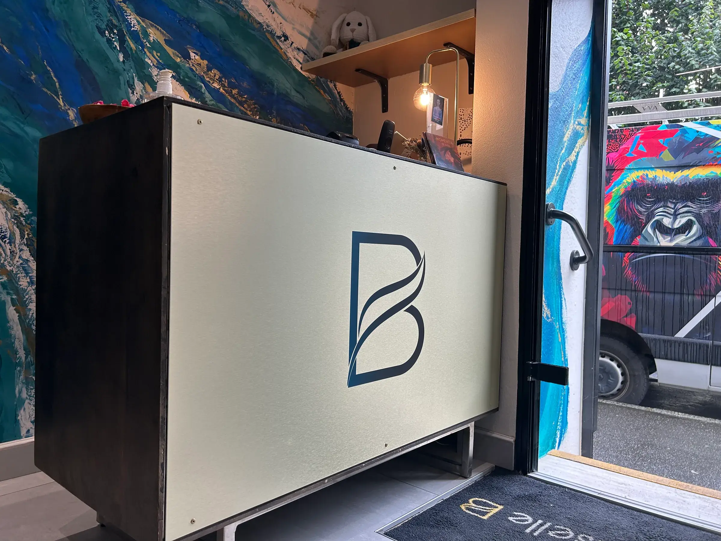 Comptoir d'accueil habillé d'une plaque en aluminium beige ornée d'un monogramme bleu marine, devant une fresque murale aux tons bleus