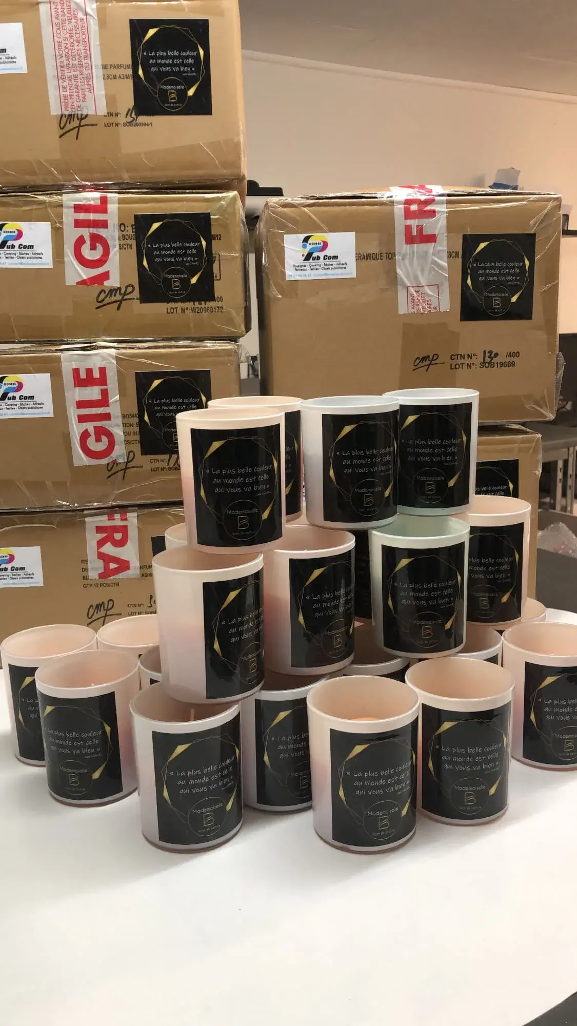 Pots roses à étiquettes noires et dorées alignés sur une table devant des cartons d'expédition empilés