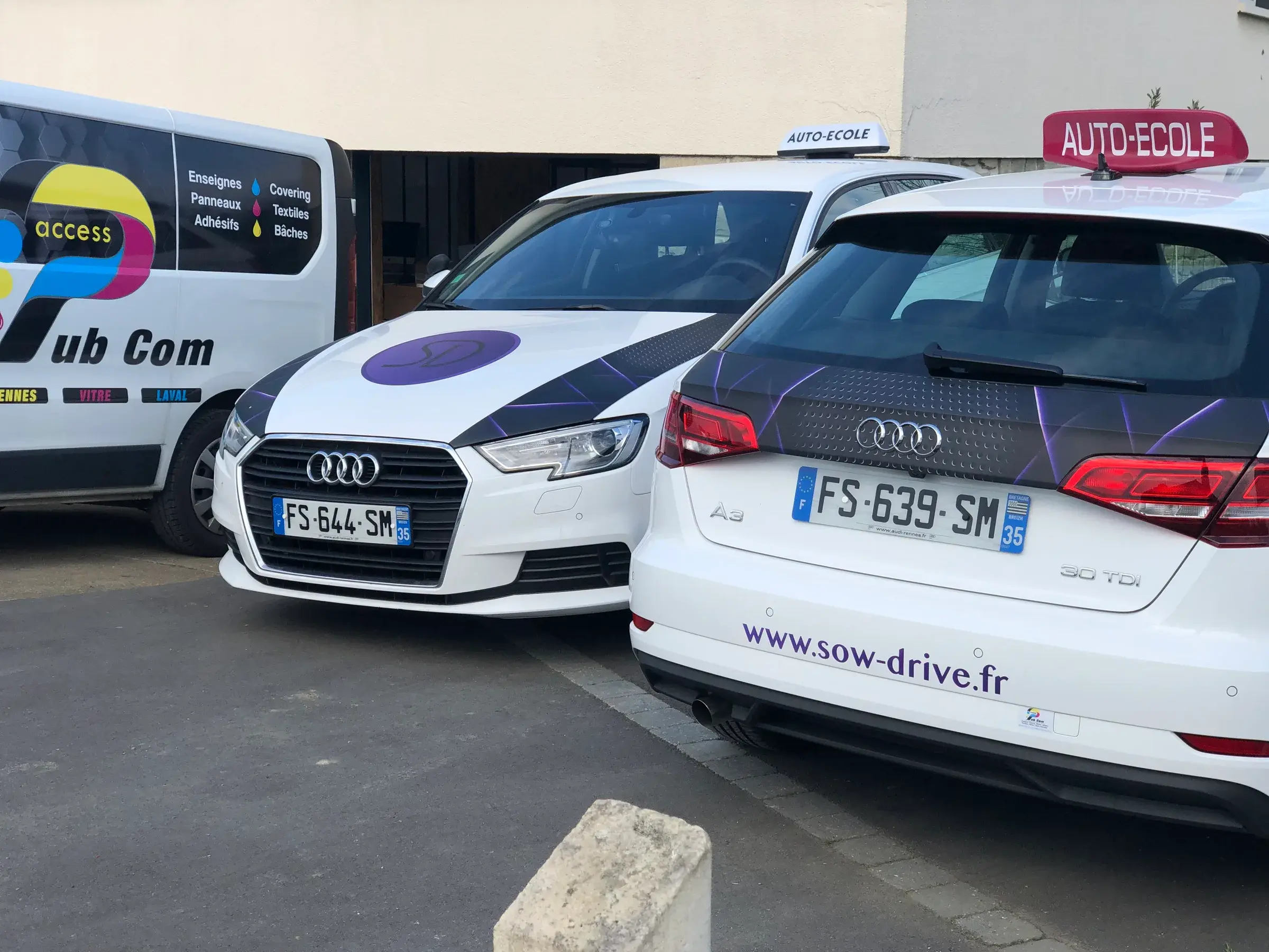 Deux voitures d'auto-école, capot et lunette arrière recouverts d'adhésif violet, garées à côté de l'utilitaire d'Access Pub Com