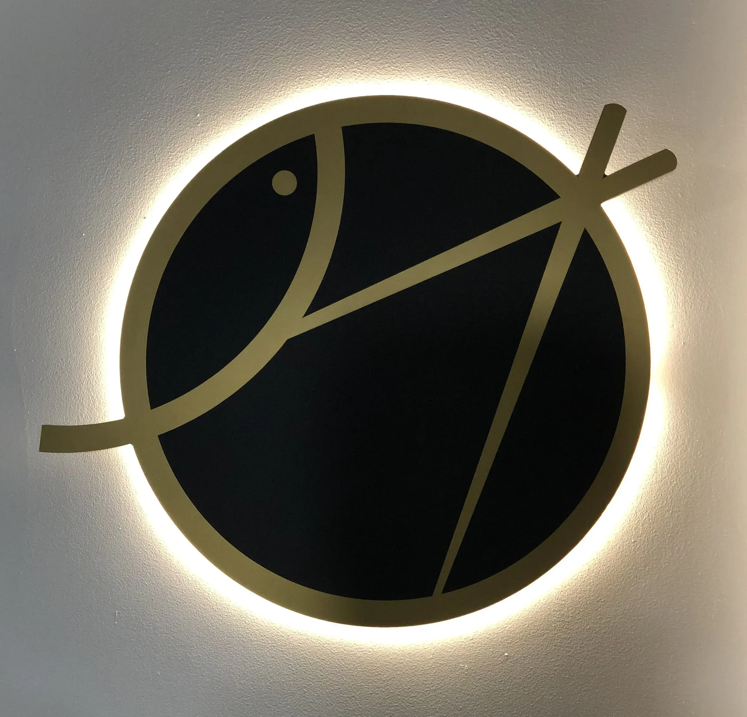 Logo circulaire noir et doré rétroéclairé, halo de lumière sur un mur blanc