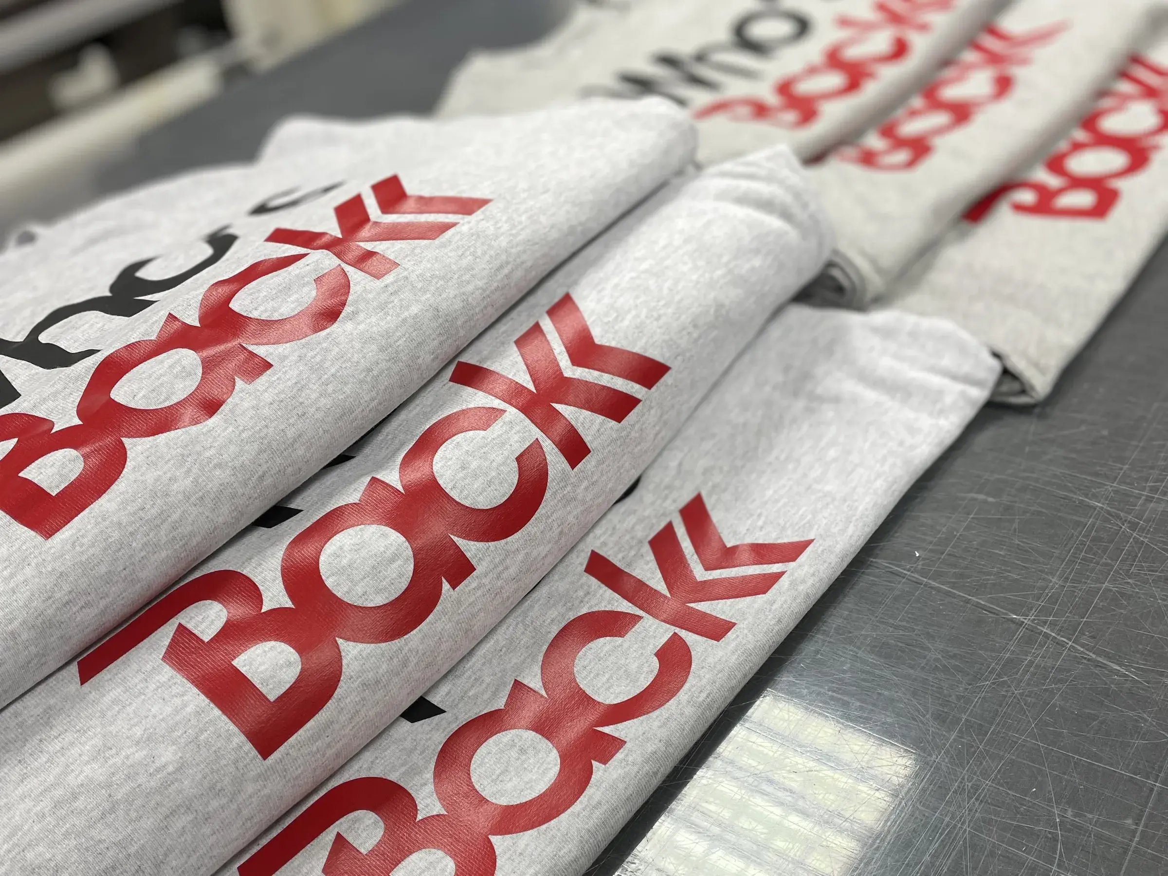 Sweats gris chinés marqués d'un logo rouge et noir, pliés et empilés sur un plan de travail