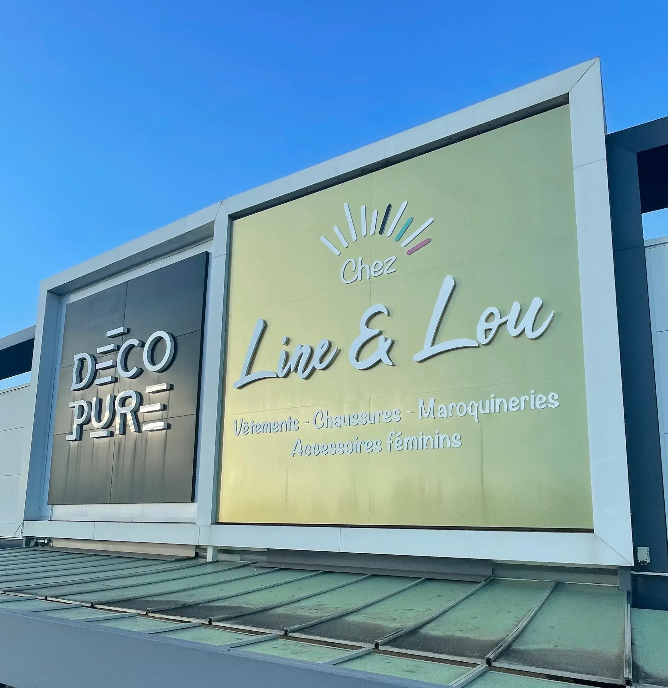 Deux caissons d'enseigne côte à côte en haut d'une façade commerciale, lettres en relief sur fond noir et sur fond doré