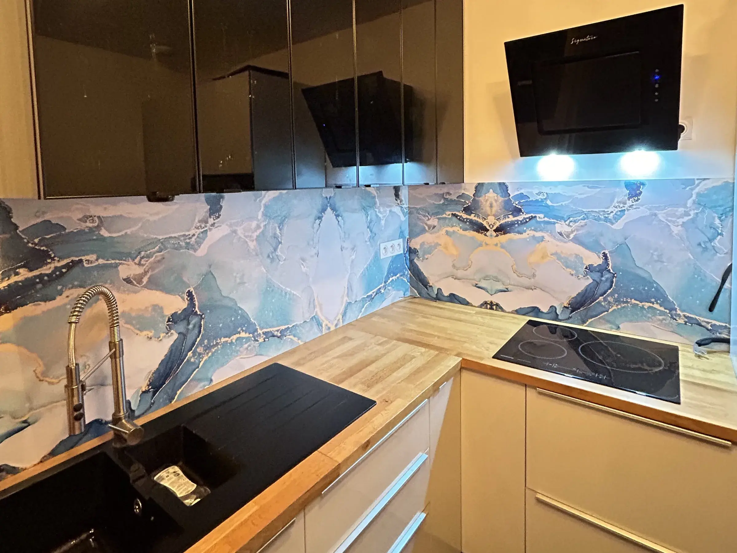 Crédence de cuisine habillée d'un panneau imprimé aux motifs de marbre bleu et blanc, entre un plan de travail en bois et des meubles hauts noirs