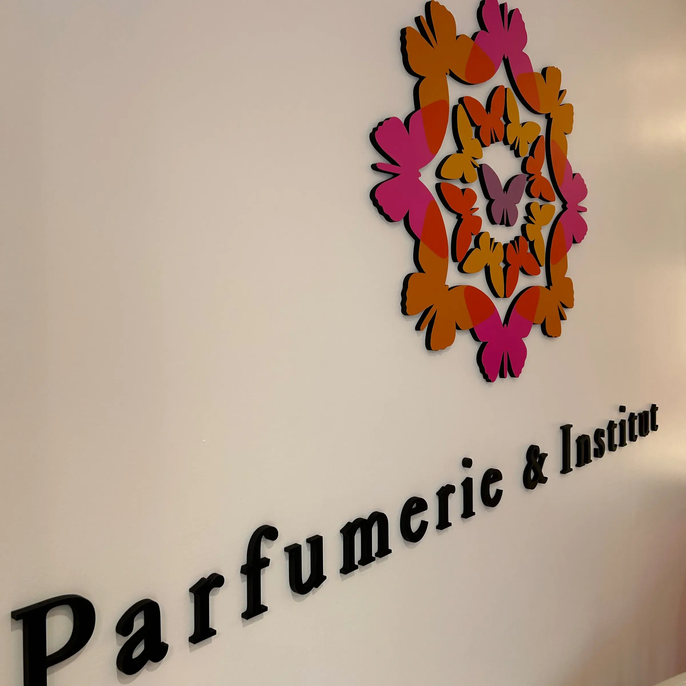 Lettres noires en relief et motif de papillons roses et orange posés sur le mur blanc d'une parfumerie