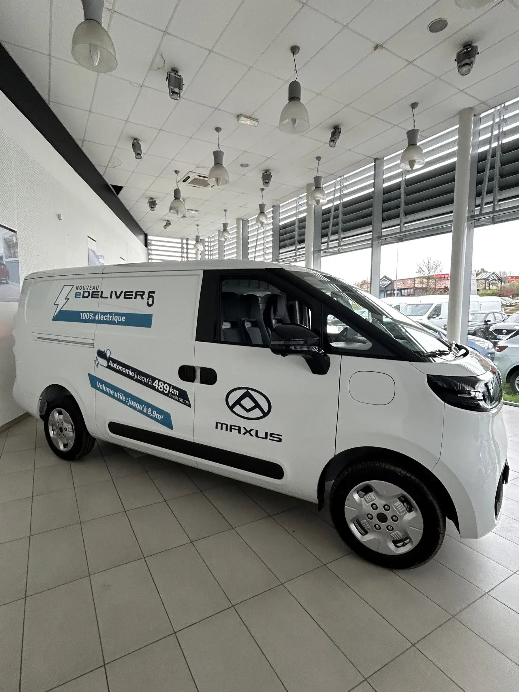 Utilitaire électrique blanc avec marquage bleu sur les flancs, exposé dans le hall d'une concession