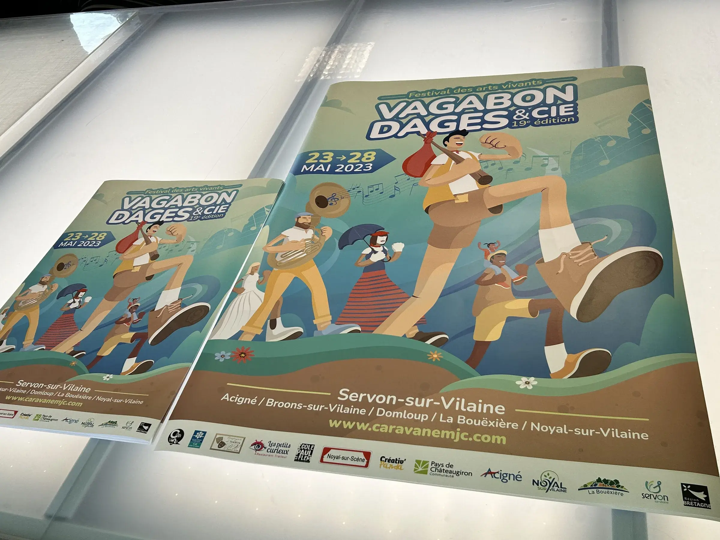 Deux affiches illustrées de personnages en marche pour un festival, en deux formats, posées sur une table blanche