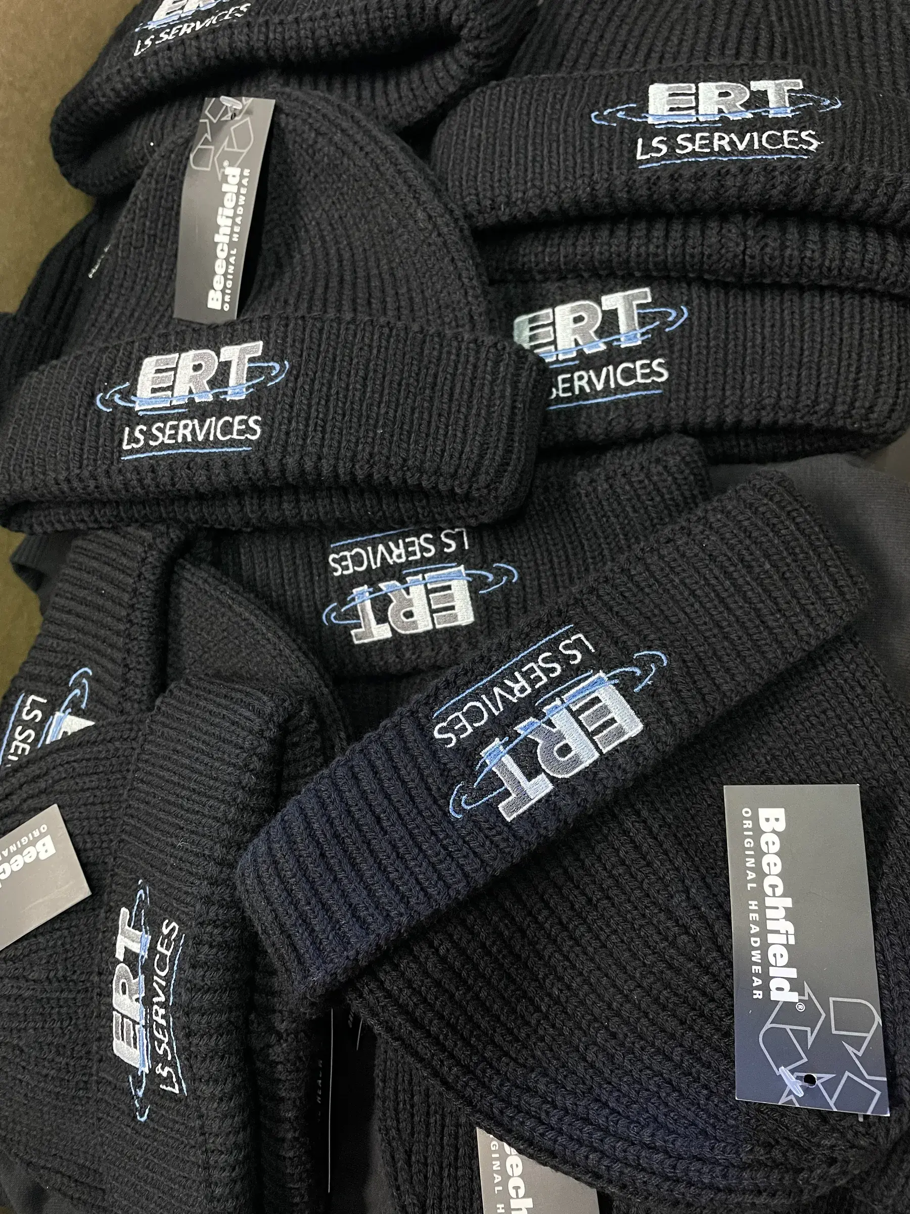 Bonnets noirs en maille brodés d'un logo bleu et blanc, empilés avec leurs étiquettes