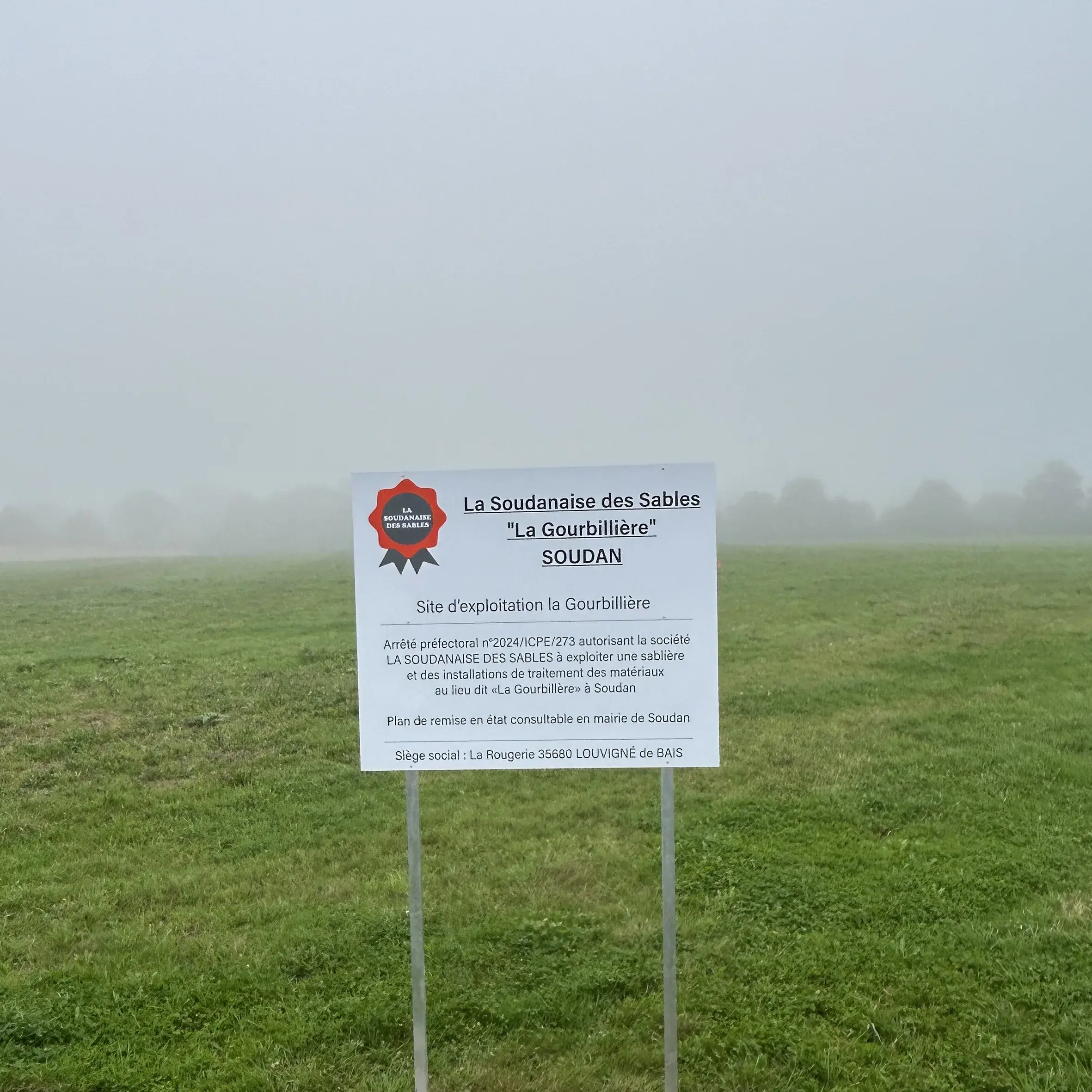 Panneau d'information réglementaire sur deux piquets dans un champ, sous la brume