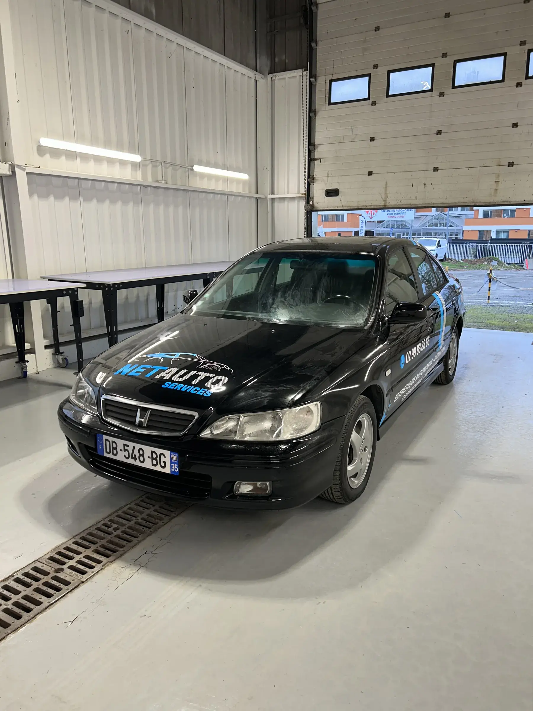 Berline noire vue de face avec logo adhésif bleu sur le capot, dans un atelier automobile