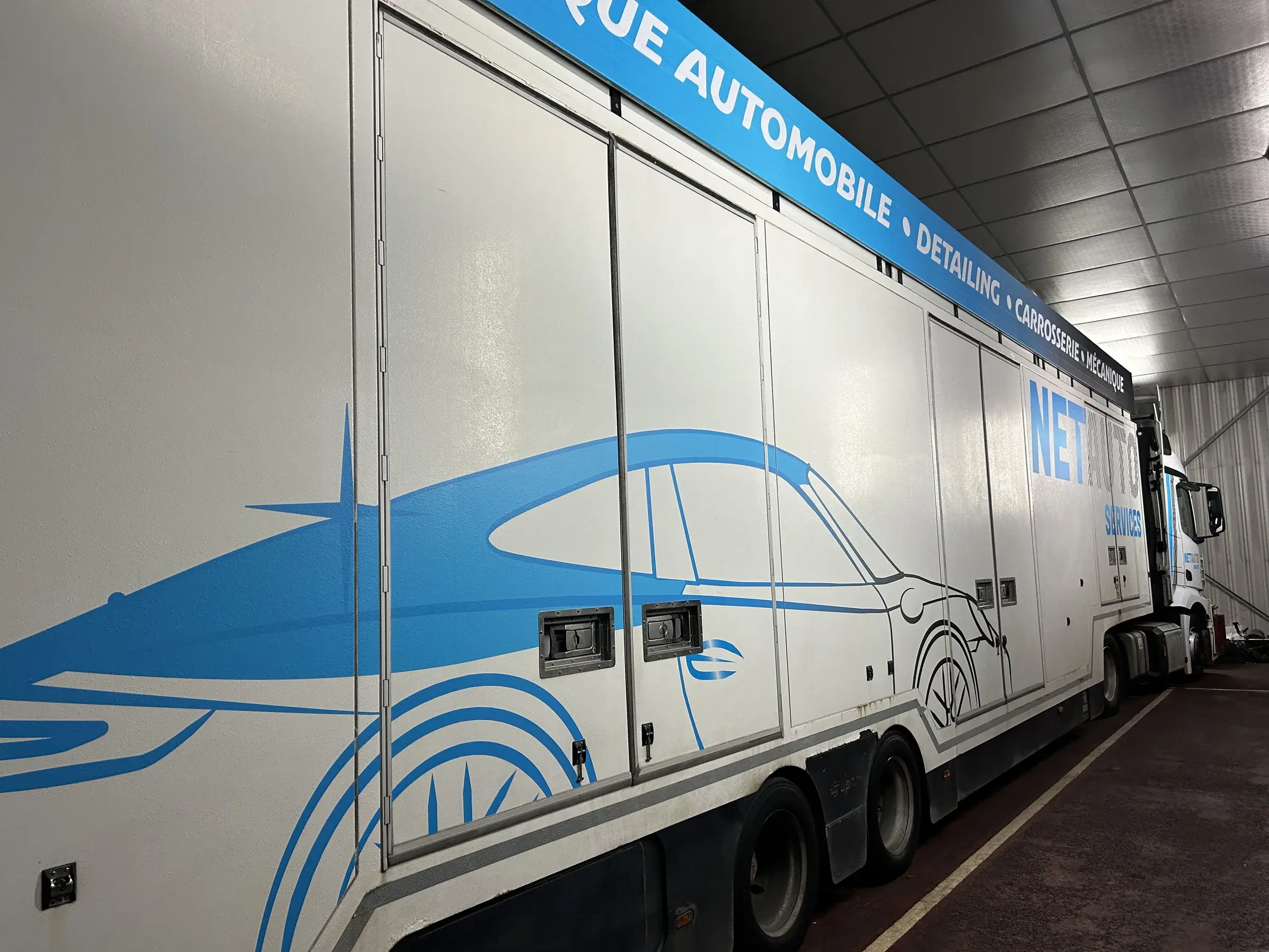 La même semi-remorque après covering, silhouette de voiture bleue et bandeau de texte sur toute la longueur du flanc
