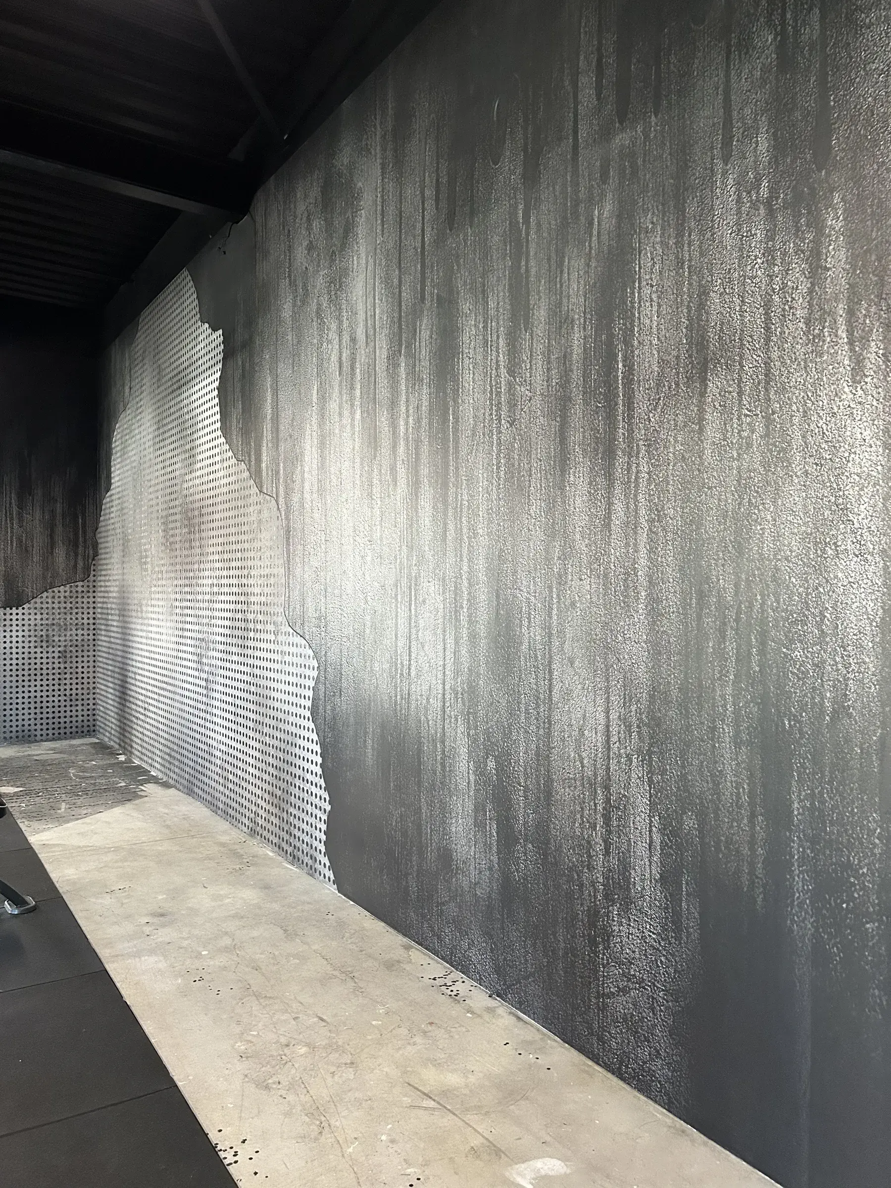 Détail d'un mur de salle de sport habillé d'un décor imprimé effet béton, avec une zone de métal perforé aux contours irréguliers
