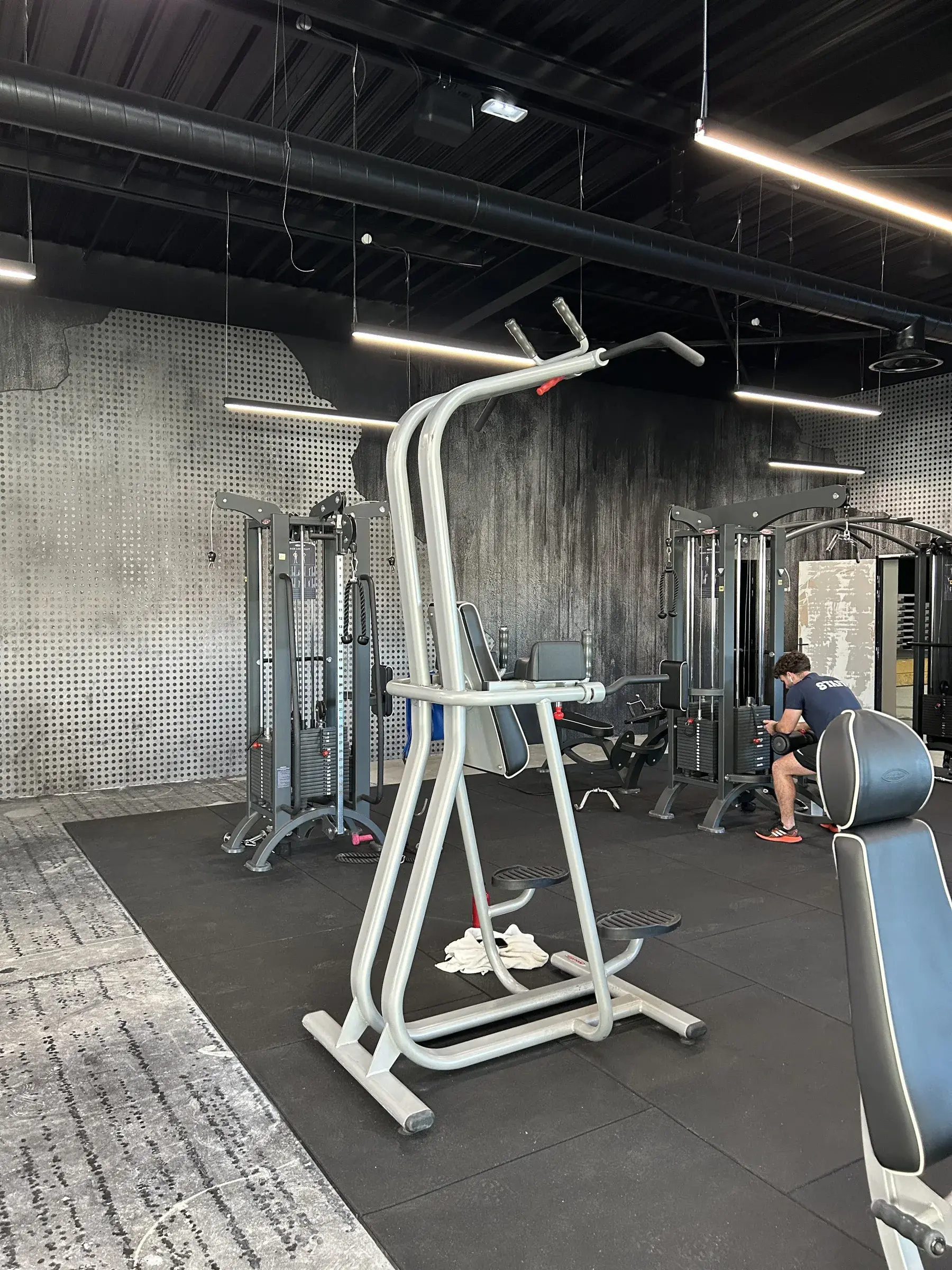 Station de traction et appareils à charge guidée dans une salle de sport aux murs habillés d'un décor imprimé effet béton et métal perforé