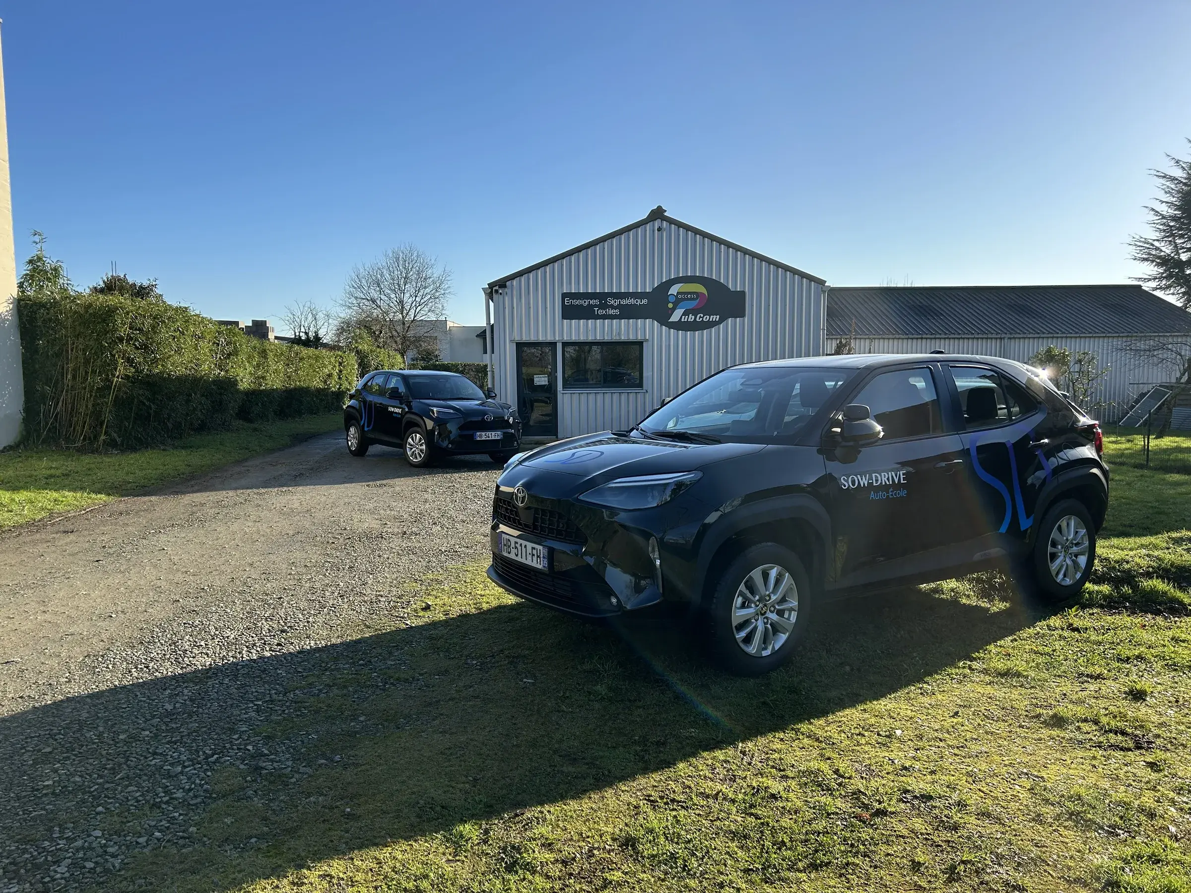 Deux SUV noirs marqués d'un monogramme bleu sur les portières, garés devant l'atelier d'Access Pub Com