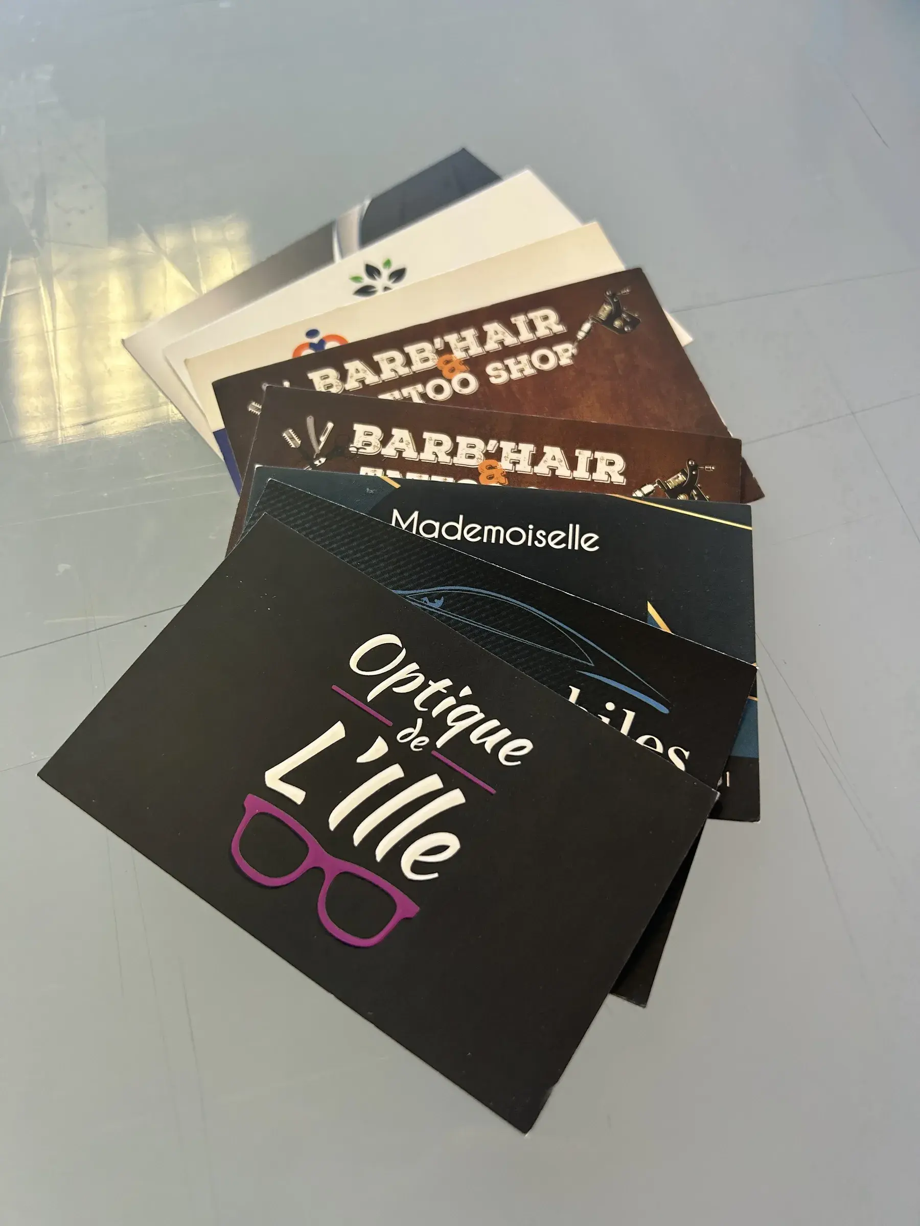 Éventail de cartes de visite noires et bleues, l'une ornée d'une paire de lunettes violettes, posé sur une table vitrée