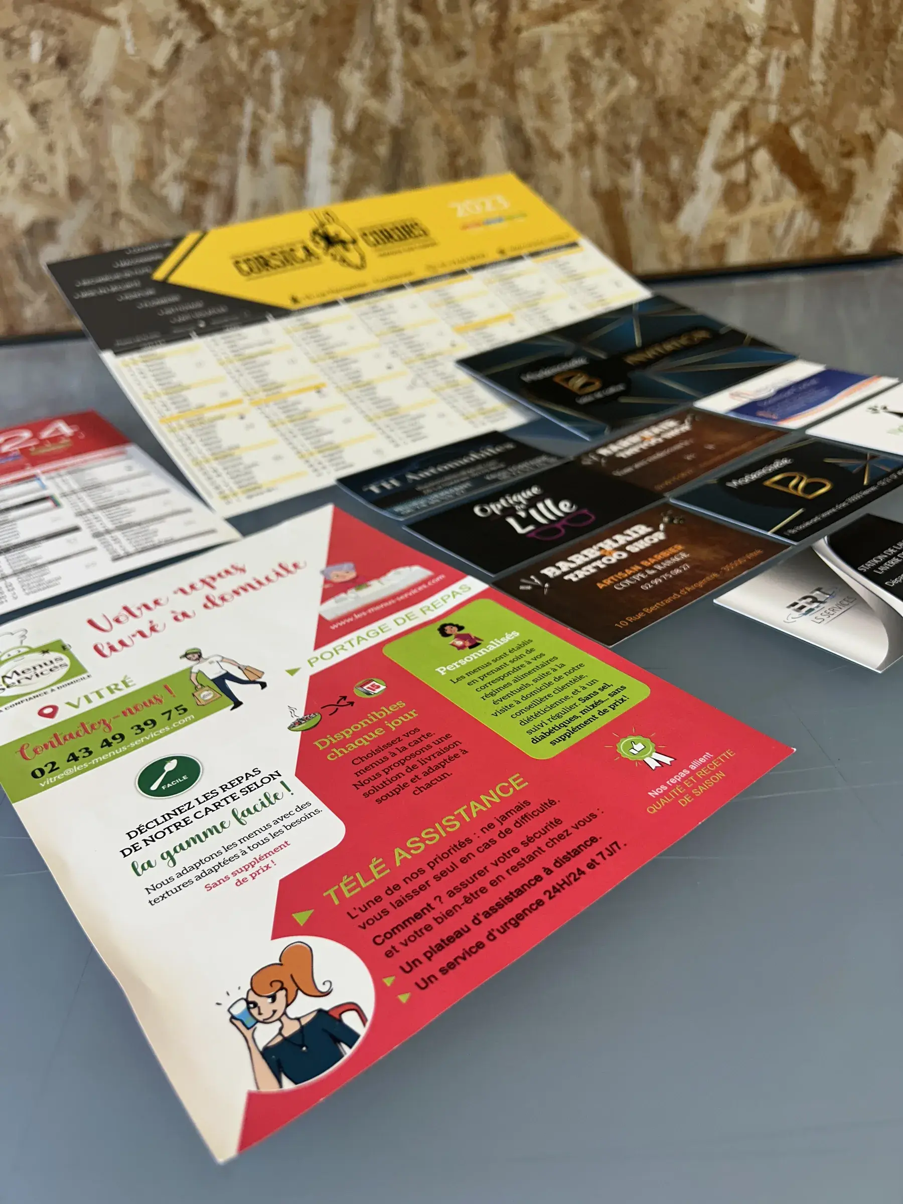 Calendrier jaune, jeu de cartes de visite noires et dépliant rouge et blanc posés en éventail sur une table grise