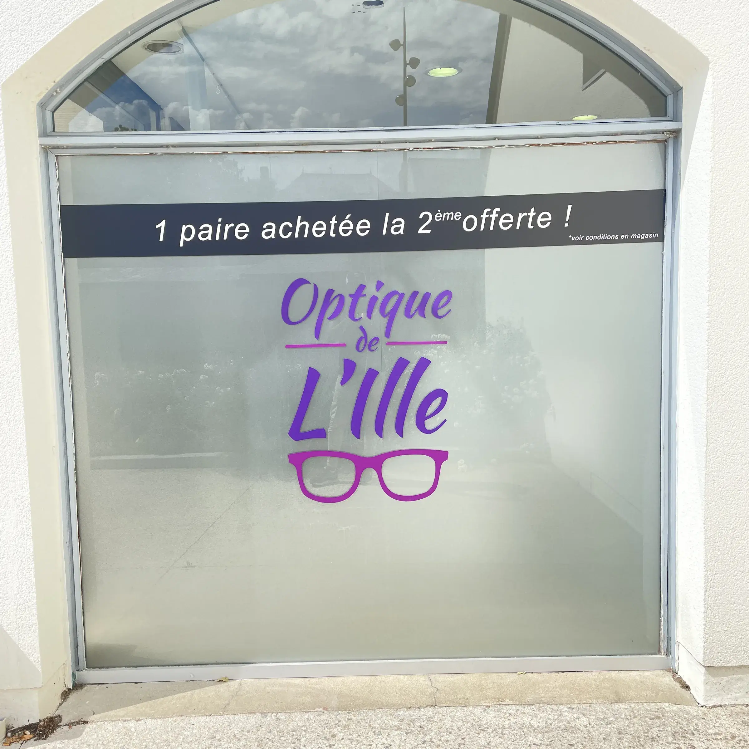 Vitrine dépolie d'un opticien avec logo adhésif violet et bandeau promotionnel noir en partie haute