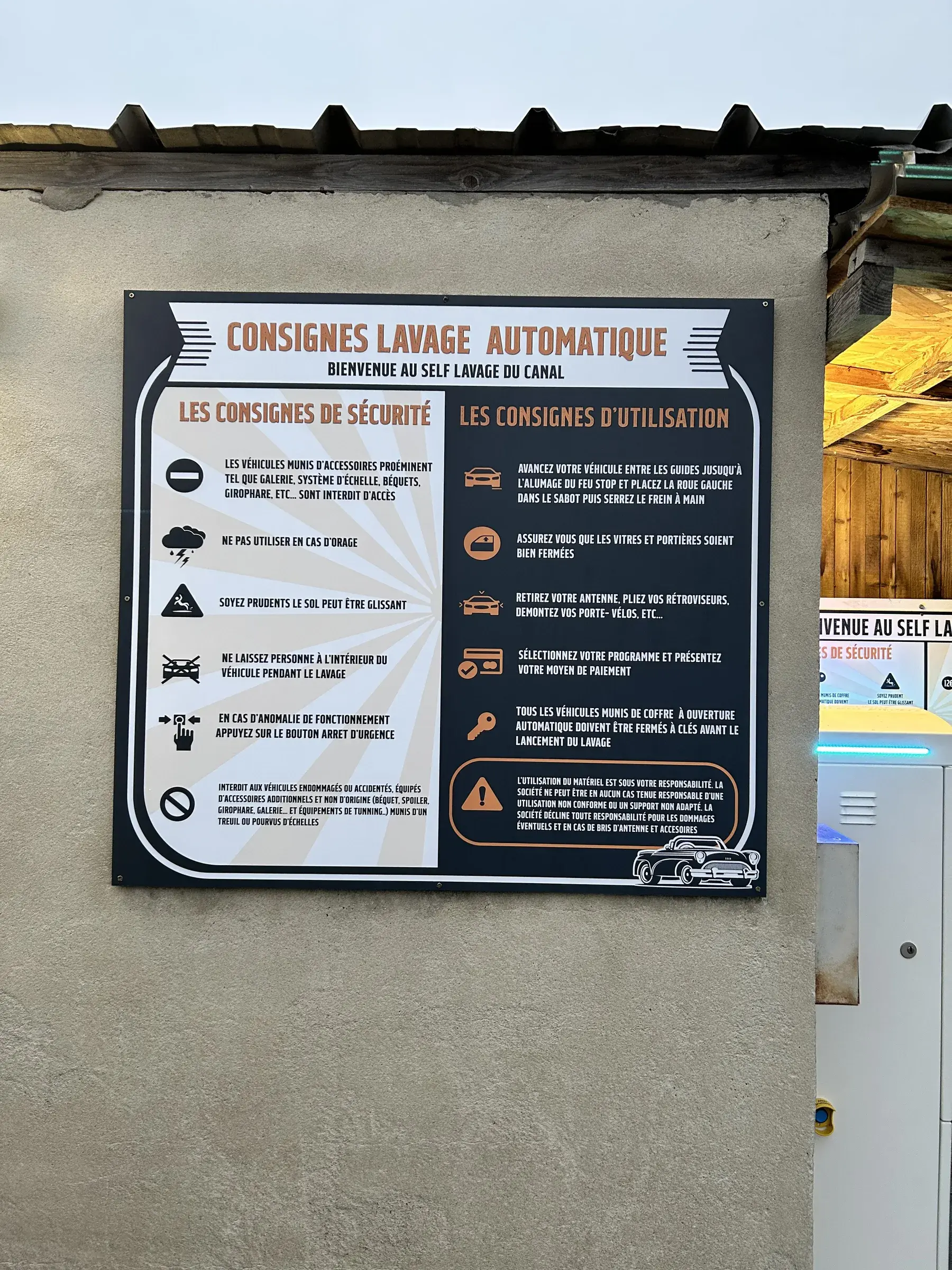 Panneau de consignes d'un lavage automatique fixé sur un mur crépi, texte orange et pictogrammes sur fond noir