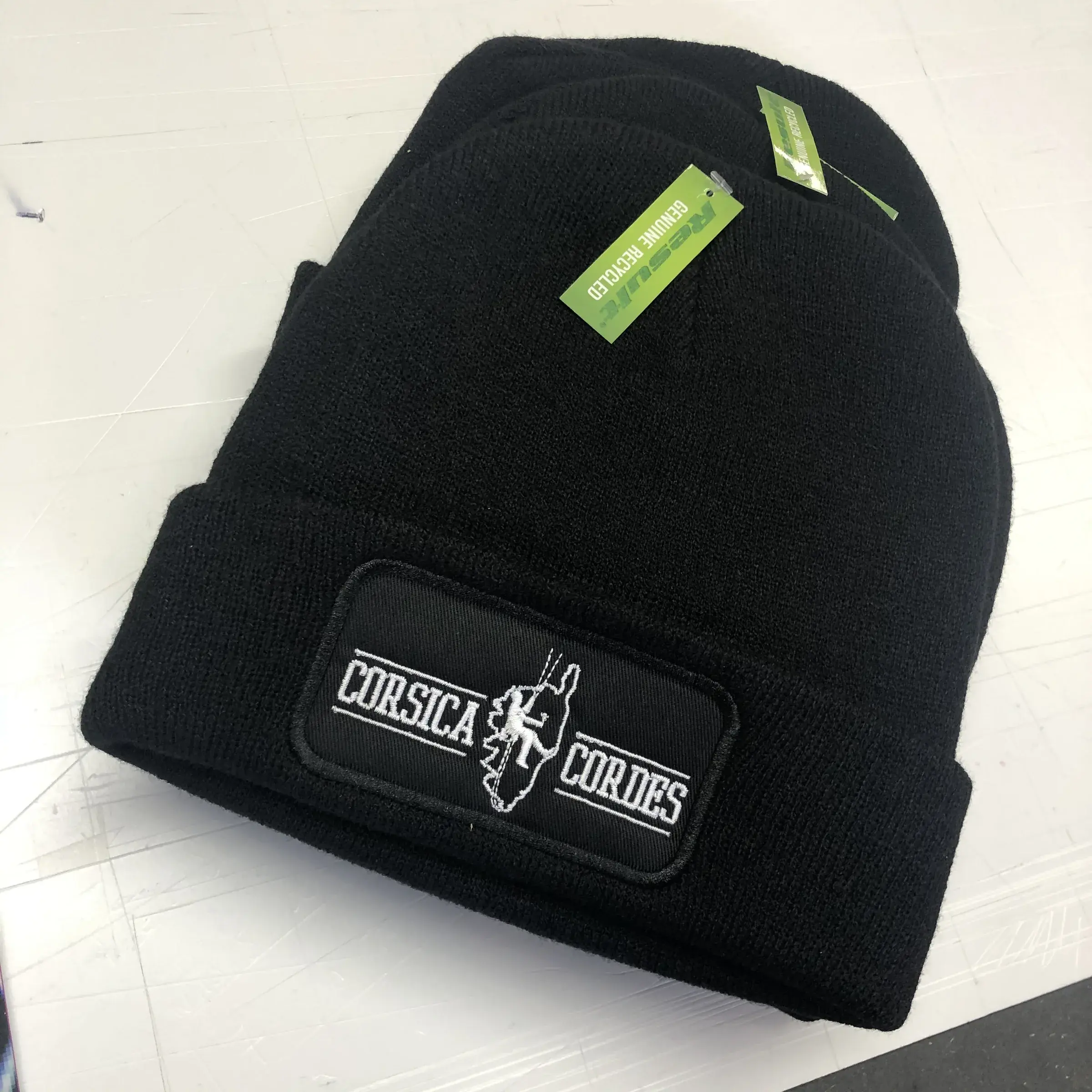Bonnets noirs à revers avec écusson brodé rectangulaire noir et blanc, empilés sur une table