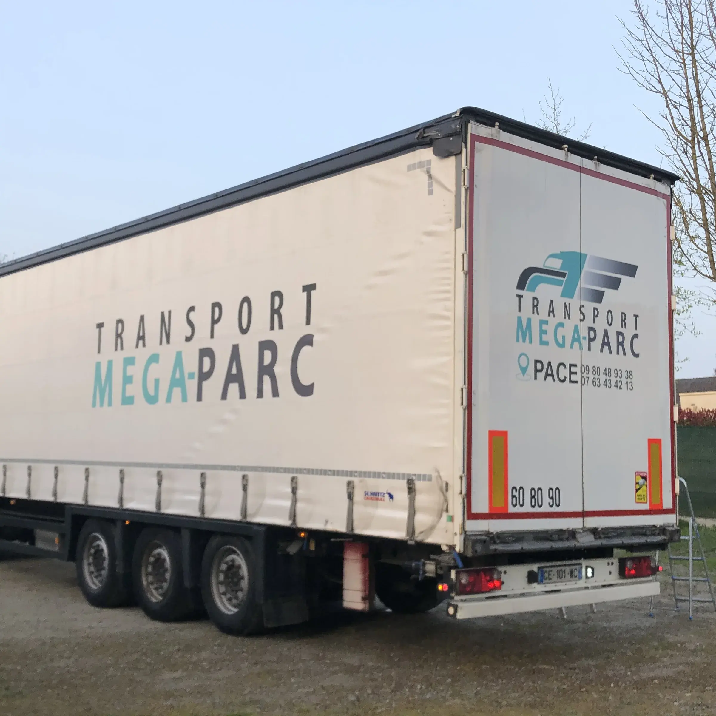 Semi-remorque bâchée avec lettrage adhésif gris et vert sur la bâche et les portes arrière, garée sur un terrain