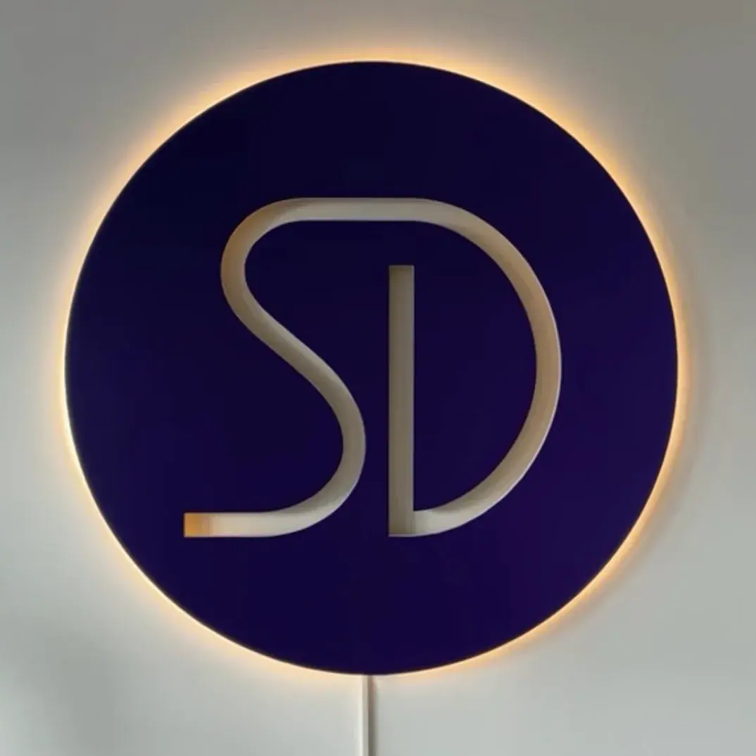 Disque violet rétroéclairé au monogramme ajouré, fixé sur un mur clair